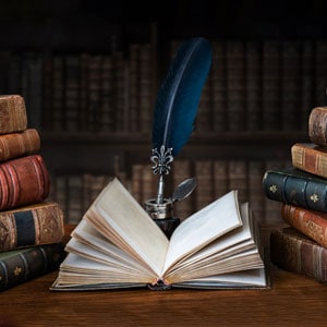 An open book with a quill and ink stand on a table surrounded by other books - Litigation Consultants